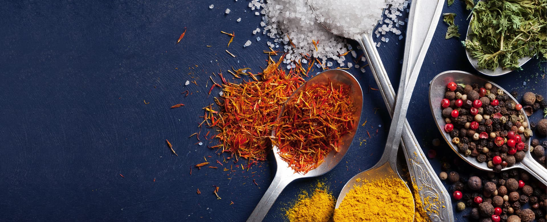A photo of coarse mountain salt, safron, assortment of red, black and green peppercorns, and dried herbs.